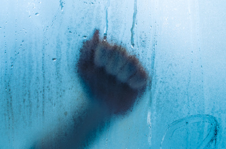 A hand fist knocks on the sweaty fogged window. Water droplets condensation background of dew on...