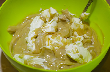 Mixing with a spoon condensed milk with butter in the green bowl. Background texture of the food ingridients of a tasty, fresh and sweet dessert. The process of making homemade snack concept.の写真素材