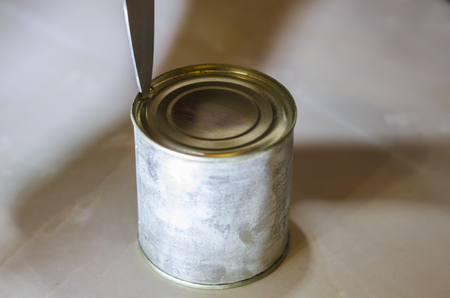 Close up view of human hands opening a tin of condensed milk with a knife isolated on the light background. Food ingridients on the kitchen table.の写真素材