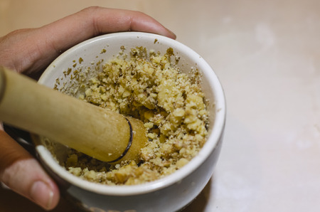 Human hand holding masher with ground walnuts in the white bowl. The process of making food concept. Chopped walnuts pile or heap on the kitchen table.の写真素材