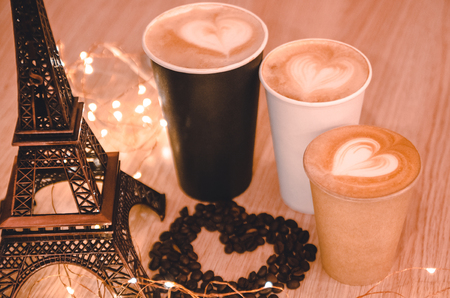 A heart made out of coffee gains on the wooden table background between Eiffel tower toy and coffee takeaway cups. A gift for your couple on Valentines day concept. Latte art with a symbol of love.の写真素材