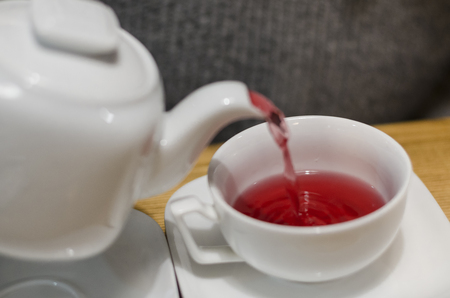 Pouring fruit red tea from the teapot into white cup concept. Eating breakfast on the wooden table background. Dinking a hot drink in the coffee shop.の写真素材