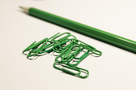 Green paperclips and a pencil  isolated on white background. Be creative concept. School supplies or stuff. Education or business background.の写真素材