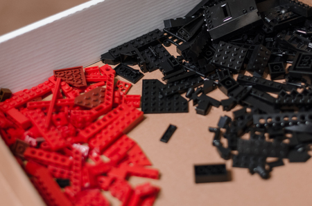 Two piles of black and red toy bricks for kids in the wooden box background. Playing in plastic toy bricks concept. Pieces and elements of constructor toys. Be creative and different.の写真素材