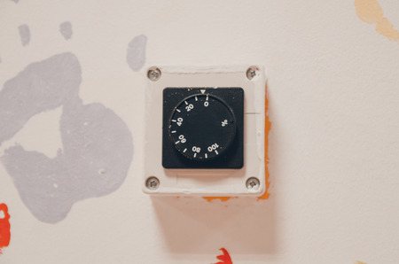 Black old thermostat on the white wall. Set the temperature in the room concept. Heating or cooling system controller.の写真素材