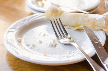 dirty plates after eating concept. White plates, glass cup and silver fork on the wooden table. Need to clean and wash the dishes.の写真素材