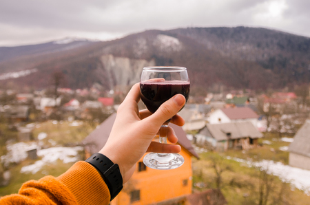 A glass of red wine in the human hand on background of mountains. Drink wine in the mountains concept. Nature landscape of spring season. Alcohol drinks.の写真素材