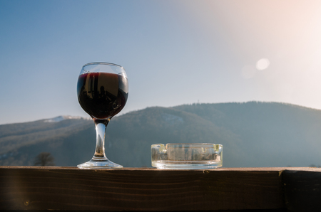 A glass of red wine and ashtray on the background of mountains. Drink wine and smoke cigarettes in the mountains concept. Nature landscape of spring season. Alcohol drinks.の写真素材