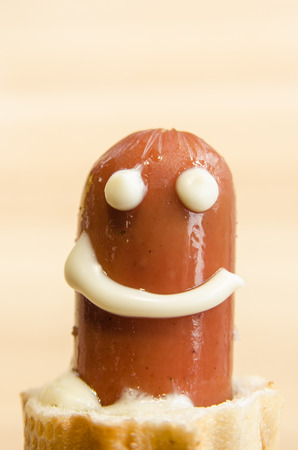 A baked hot dog in the human hand. Junk food concept. Freshly made sausage in dough with melted cheese. Eat tasty. A smiling face made with mayonnaise.の写真素材