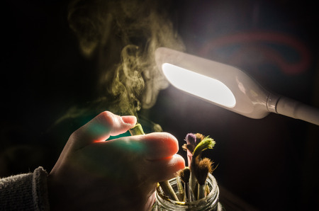Color brushes in the jar with a shining light behind. Dry paint going out of the old brush. Art equipment for drawing. Painting background with light highlights and rays.の写真素材
