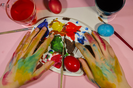painter hands coloring eggs with a palette with colors concept. Easter background. Be creative in...