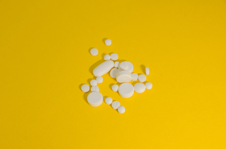 White medical pills on the yellow background. Medicine concept. Cure your pain with capsules...