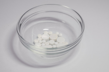 White medical pills in the glass bowl on the white background. Medicine concept. Cure your pain with...