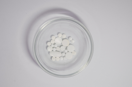 White medical pills in the glass bowl on the white background. Medicine concept. Cure your pain with capsules treatment. Stay healthy and take tabletsの写真素材