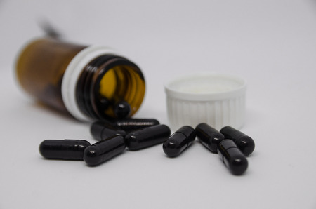 Medical black pills spilling out of pill bottle. Medicine concept isolated on the white background. Cure your pain with capsules treatment. Stay healthy and take tabletsの写真素材