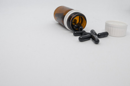 Medical black pills spilling out of pill bottle. Medicine concept isolated on the white background....