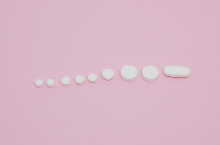 Medical pills in a line ascending. Medicine concept isolated on the pink background. Cure your pain with capsules treatment. Stay healthy and take tabletsの写真素材