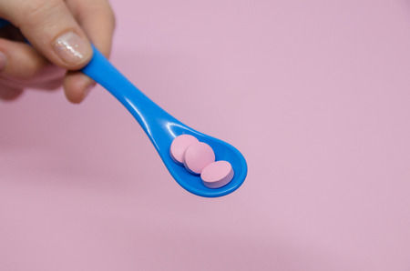 Medical pink pills in a spoon in the human hand. Medicine concept isolated on the rose background....