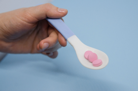Medical pink pills in a spoon in the human hand. Medicine concept isolated on the blue background....