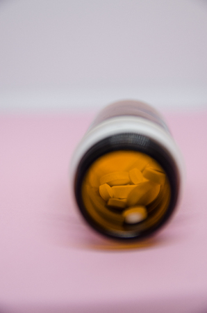Medical pills spilling out of pill bottle. Medicine concept isolated on the pink background. Cure your pain with capsules treatment. Stay healthy and take tabletsの写真素材
