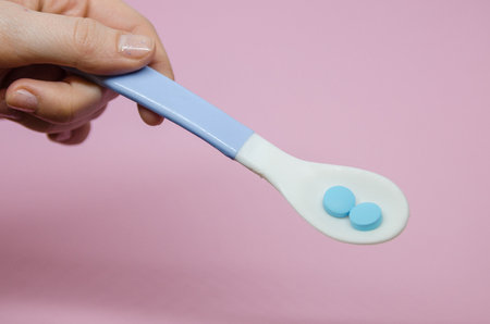 Medical blue pills in a spoon in the human hand. Medicine concept isolated on the rose background. Cure your pain with capsules treatment. Stay healthy and take tabletssの写真素材