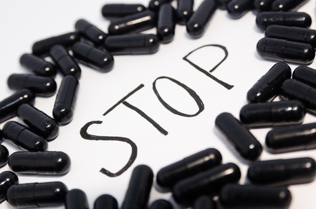 Medical black pills in the circle with written word Stop. Medicine concept isolated on the white background. Cure your pain with capsules treatment. Stay healthyの写真素材