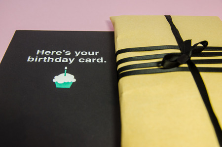 A handmade gift in brown wrapping paper and with black ribbon. A present with a postcard for...