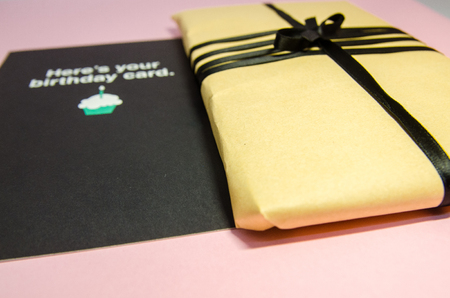 A handmade gift in brown wrapping paper and with black ribbon. A present with a postcard for birthday close up view. Texture background of a holiday preparations.の写真素材