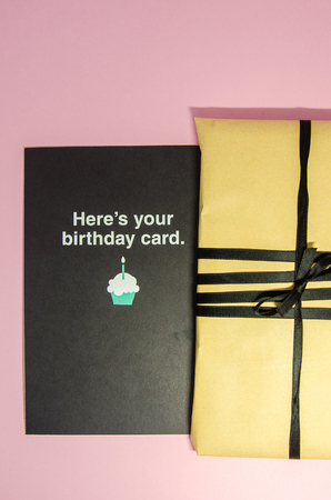 A handmade gift in brown wrapping paper and with black ribbon. A present with a postcard for birthday close up view. Texture background of a holiday preparations.の写真素材