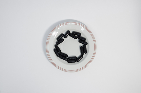 Medical black pills in the circle on the plate. Medicine concept isolated on the white background. Cure your pain with capsules treatment. Stay healthyの写真素材