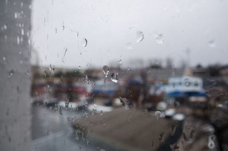 view on the street through the window with rain drops from the room. Rainy and cold weather outside. Water drops on the glass with blurry backgroundの写真素材