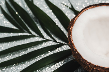 Ripe coconut composition background. A half of fresh coconut with a tropical palm leaf on shiny...