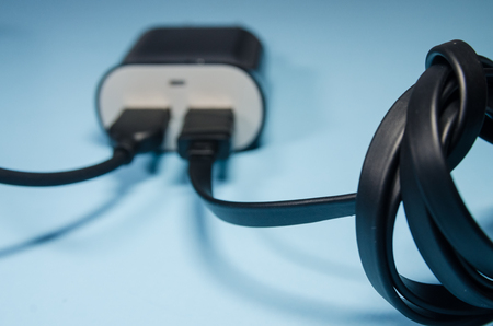 Black charging block with two cords for a mobile phone on blue background. Keep the battery charged on your device anyway you go. Technology connect with  USB electrical plug close up.の写真素材