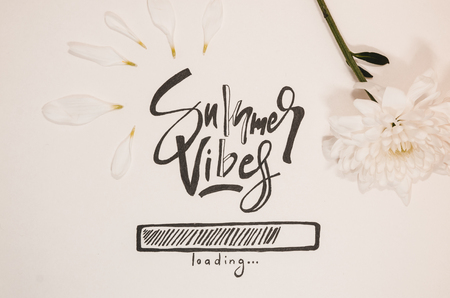 Hello summer concept.  A white paper where is wtitten with nice handwriting - Summer vibes loading. Summer quote background and a white flowerの写真素材