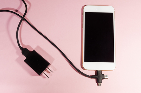 Usb black cable with three different point ends charging a mobile phone isolated on pink background. Technology connect close up. Charge diffrent types of devices with one cord.の写真素材
