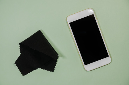 cleaning smartphone with a microfiber cloth concept. A black cleaner for mobile phone isolated on green background.の写真素材