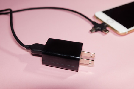 Usb black cable with three different point ends charging a mobile phone isolated on pink background. Technology connect close up. Charge diffrent types of devices with one cord.の写真素材