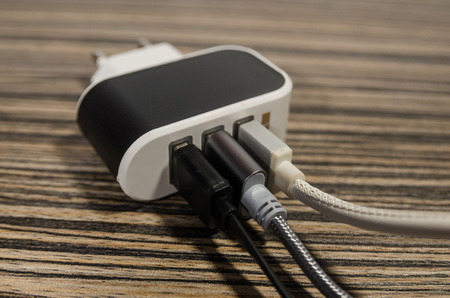 White charging block with three phone cables on wooden table background. Keep the battery charged on your devices concept. Technology connect with USB electrical plug close up.の写真素材
