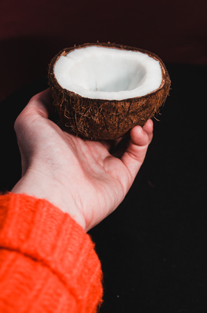 A hand holding rape half of the coconut concept. A half of fresh coconut on black background . White exotic fruit close upの写真素材