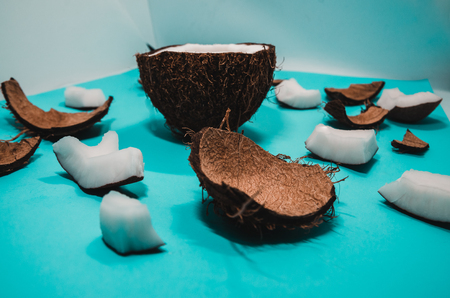 Ripe coconut composition background. A half of fresh coconut with cracked pieces of hairy peel on blue surface. White exotic fruit close upの写真素材