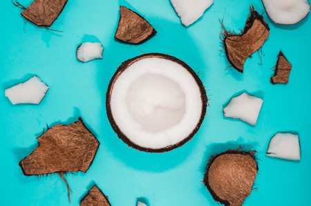 Ripe coconut composition background. A half of fresh coconut with cracked pieces of hairy peel on blue surface. White exotic fruit from the top viewの写真素材