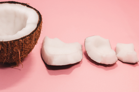 Ripe coconut composition background. A half of fresh coconut with little pieces in ascending order on pink surface. White exotic fruit close upの写真素材