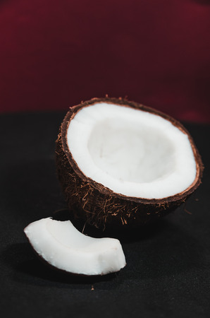 Ripe coconut composition background. A half of fresh coconut with little piece of it on black surface. White exotic fruit close upの写真素材
