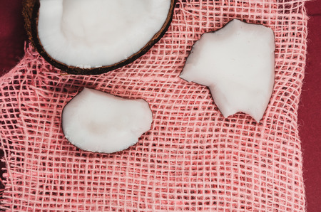 Ripe coconut composition background. A half of fresh coconut with little pieces of it on pink canvas. White exotic fruit close upの写真素材
