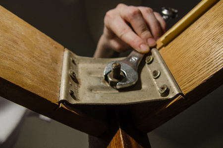 A man repairing one old wooden table at home. Repair or overhaul background. tighten the screw-nut with wrench tool concept.の写真素材