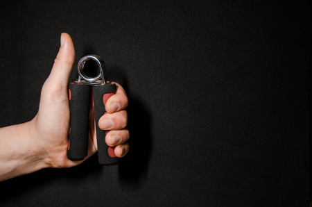 The simulator for increasing the strength of the hand, the expander for hands. Fitness trainer in the palm on a spring mechanism. Sport and workout concept on black background.の写真素材