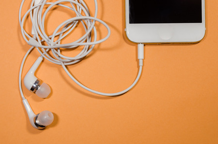 a phone with white headphones on orange background. listen to music on your device anyway you go...