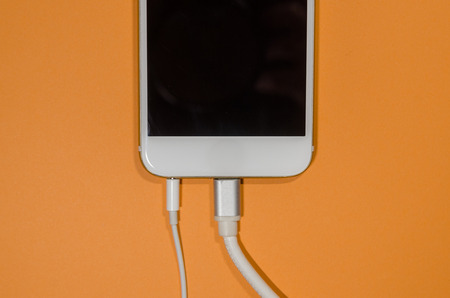 a phone with white usb cable and headphones on orange background with copy space. Keep the battery...
