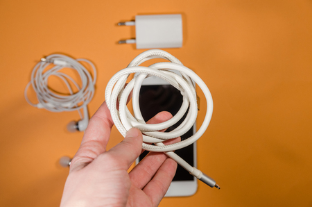 a phone with white usb cable, block and headphones on orange background. Keep the battery charged and listen to music on your device anyway you go. Tehnology connect close up.の写真素材