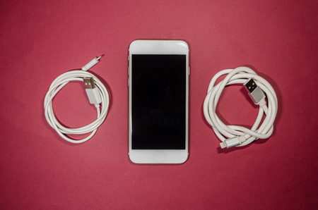 a phone with two usb cables on red background. Keep the battery charged on your device anyway you go. Technology connect close up.の写真素材